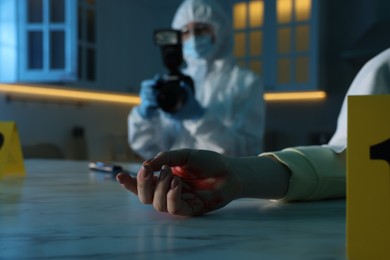 Forensic expert with camera working at crime scene and dead woman's body indoors, selective focus