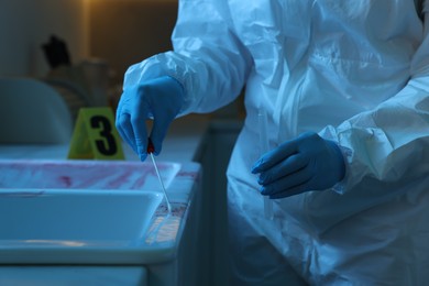 Photo of Forensic expert taking blood sample at crime scene indoors, closeup