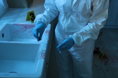 Photo of Forensic expert taking blood sample at crime scene indoors, closeup