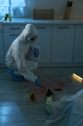 Photo of Forensic expert taking fingerprints with brush from gun and dead body at crime scene indoors