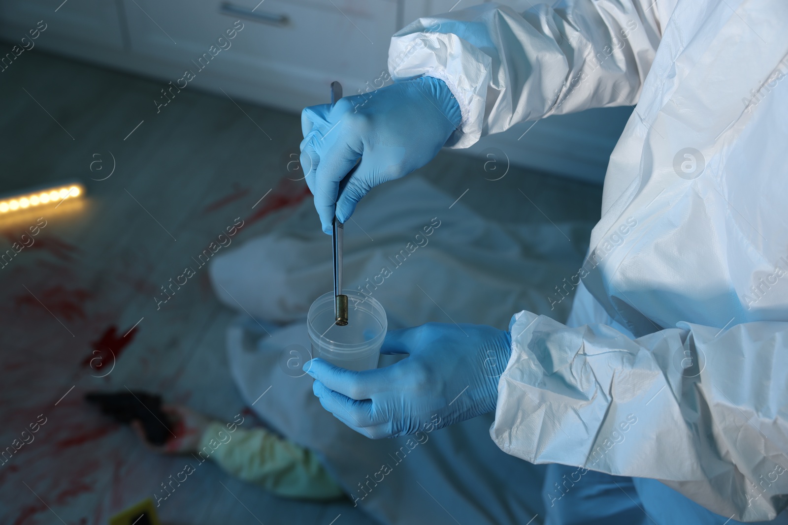 Photo of Forensic expert collecting bullet shell into container and dead body at crime scene indoors, closeup