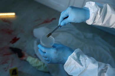 Photo of Forensic expert collecting bullet shell into container and dead body at crime scene indoors, closeup