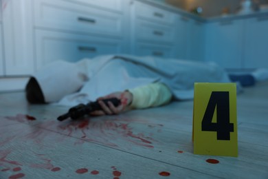 Photo of Dead body with gun at crime scene indoors, focus on numbered marker stand