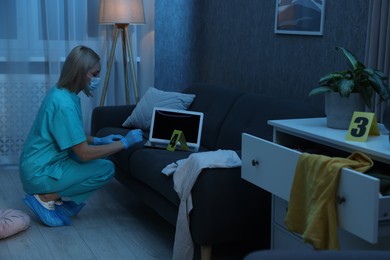 Photo of Forensic expert taking fingerprints with brush from laptop at crime scene in messy room