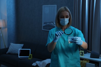 Forensic expert examining plastic bag with drug powder through magnifying glass at crime scene indoors. Space for text