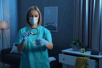 Forensic expert examining plastic bag with drug powder through magnifying glass at crime scene indoors. Space for text