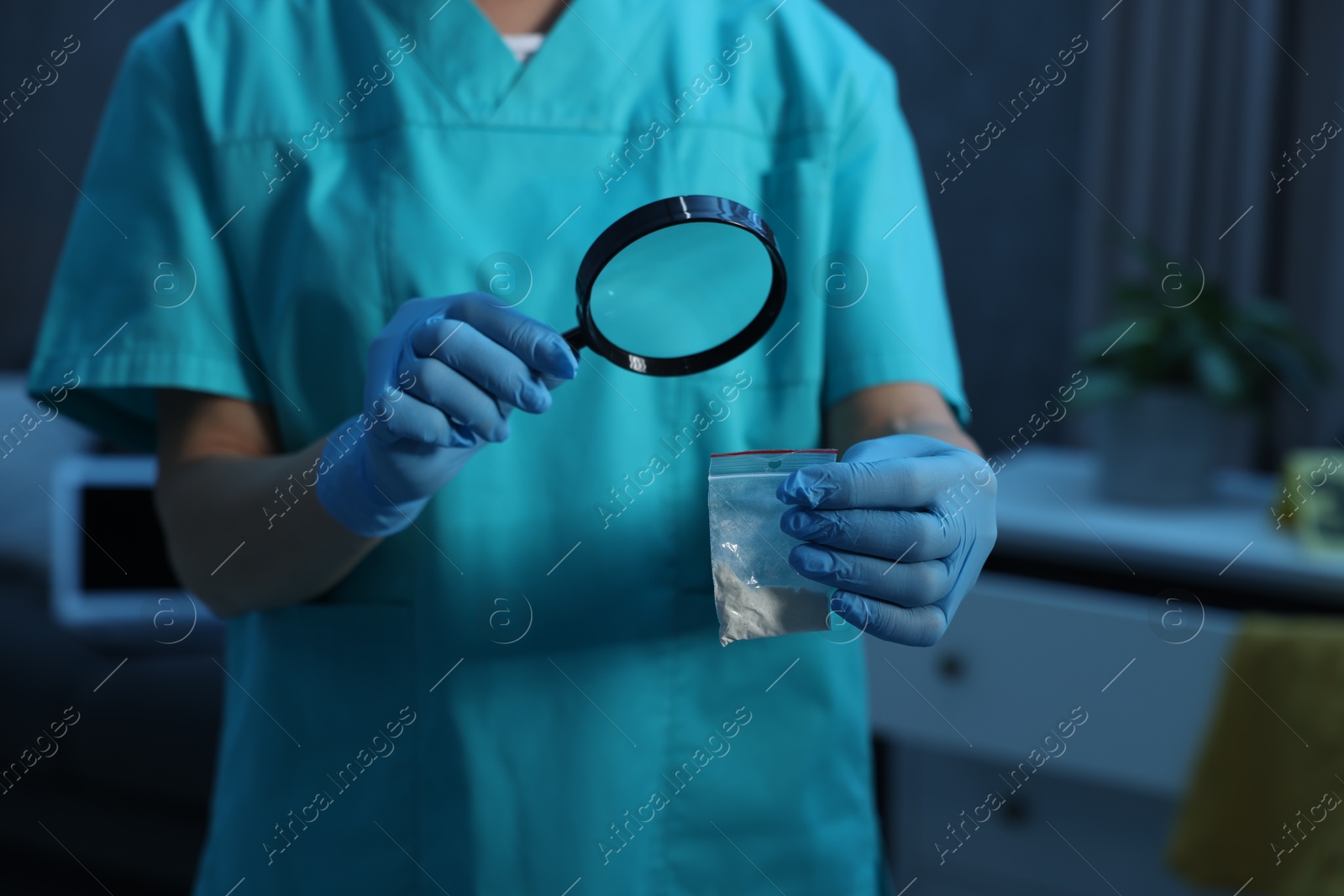 Photo of Forensic expert examining plastic bag with drug powder through magnifying glass at crime scene indoors, closeup