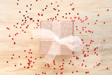 Romantic gift and confetti in shape of hearts on light wooden table, flat lay. Happy Valentine's day