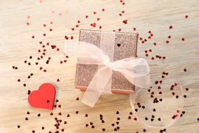 Romantic gift and confetti in shape of hearts on light wooden table, flat lay. Happy Valentine's day