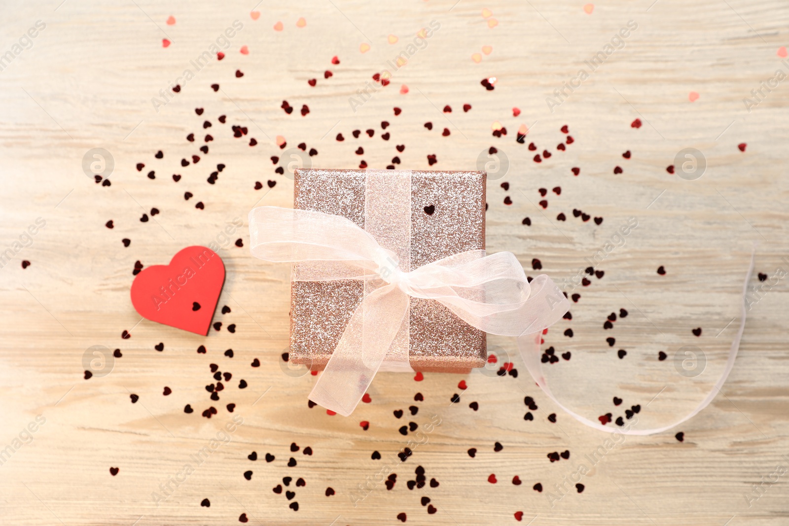 Photo of Romantic gift and confetti in shape of hearts on light wooden table, flat lay. Happy Valentine's day