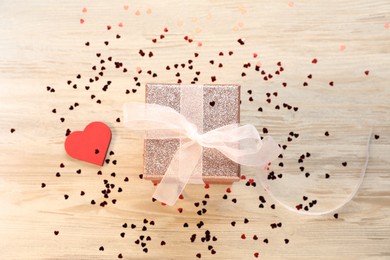 Photo of Romantic gift and confetti in shape of hearts on light wooden table, flat lay. Happy Valentine's day