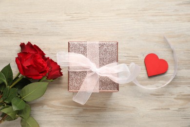 Romantic gift, roses and decorative heart on light wooden table, flat lay. Happy Valentine's day