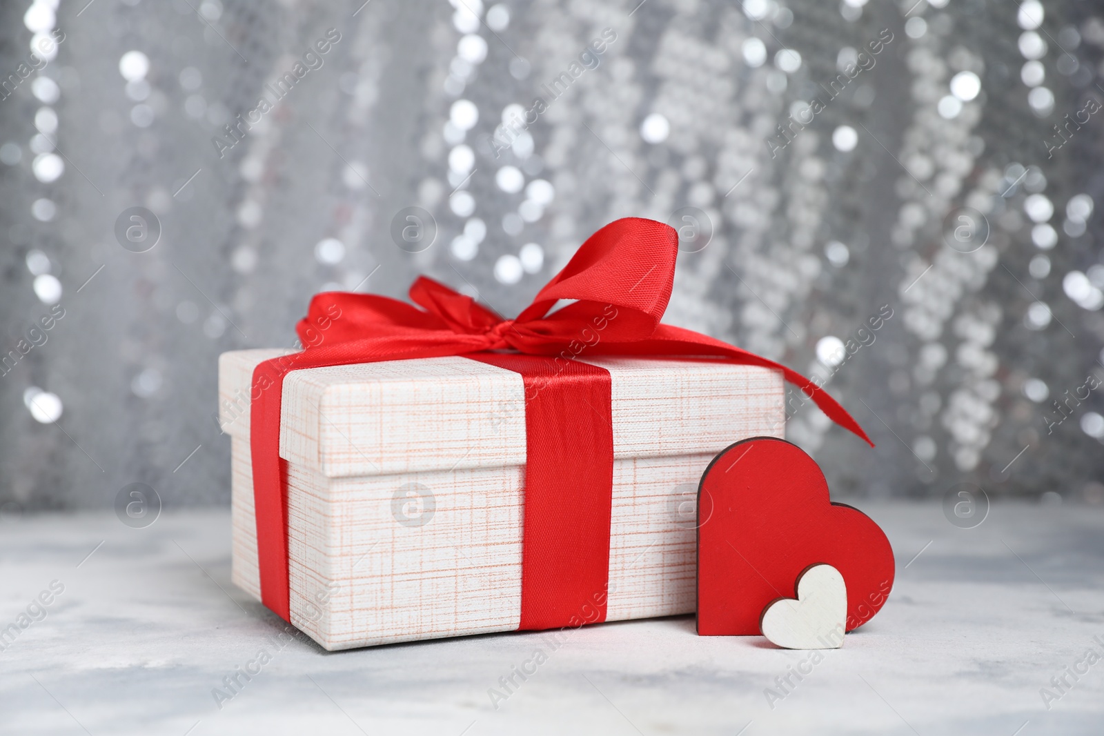 Photo of Romantic gift and decorative hearts on table against silver glitter background