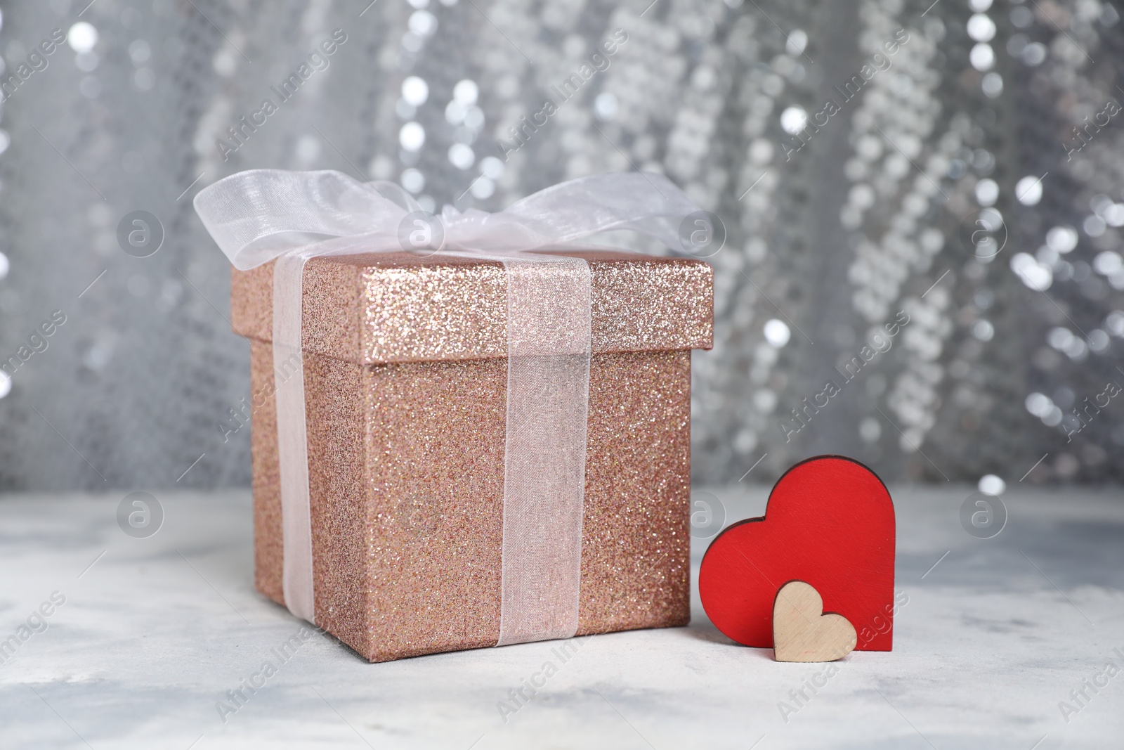 Photo of Romantic gift and decorative hearts on table against silver glitter background