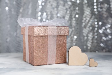 Romantic gift and wooden hearts on table against silver glitter background