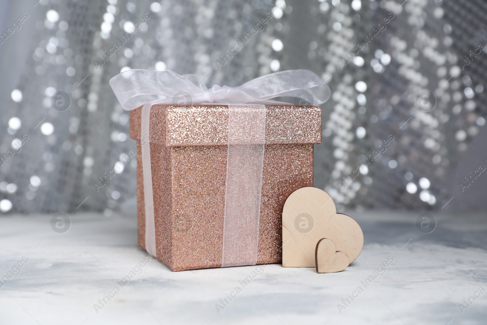 Photo of Romantic gift and wooden hearts on table against silver glitter background