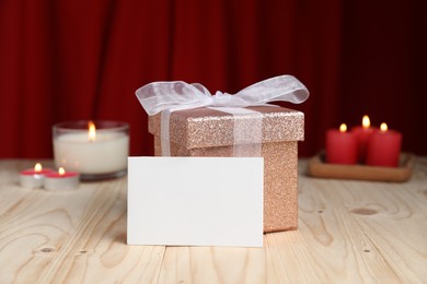 Photo of Beautiful gift box, blank card and burning candles on wooden table. Romantic present