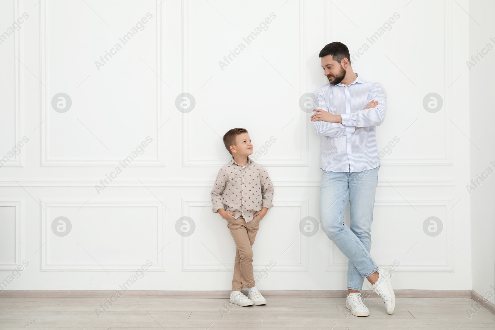 Photo of Father and his cute little son near white wall indoors, space for text