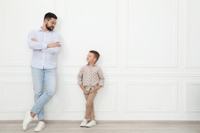 Photo of Father and his cute little son near white wall indoors, space for text