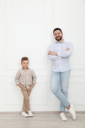 Photo of Happy father and his cute little son near white wall indoors