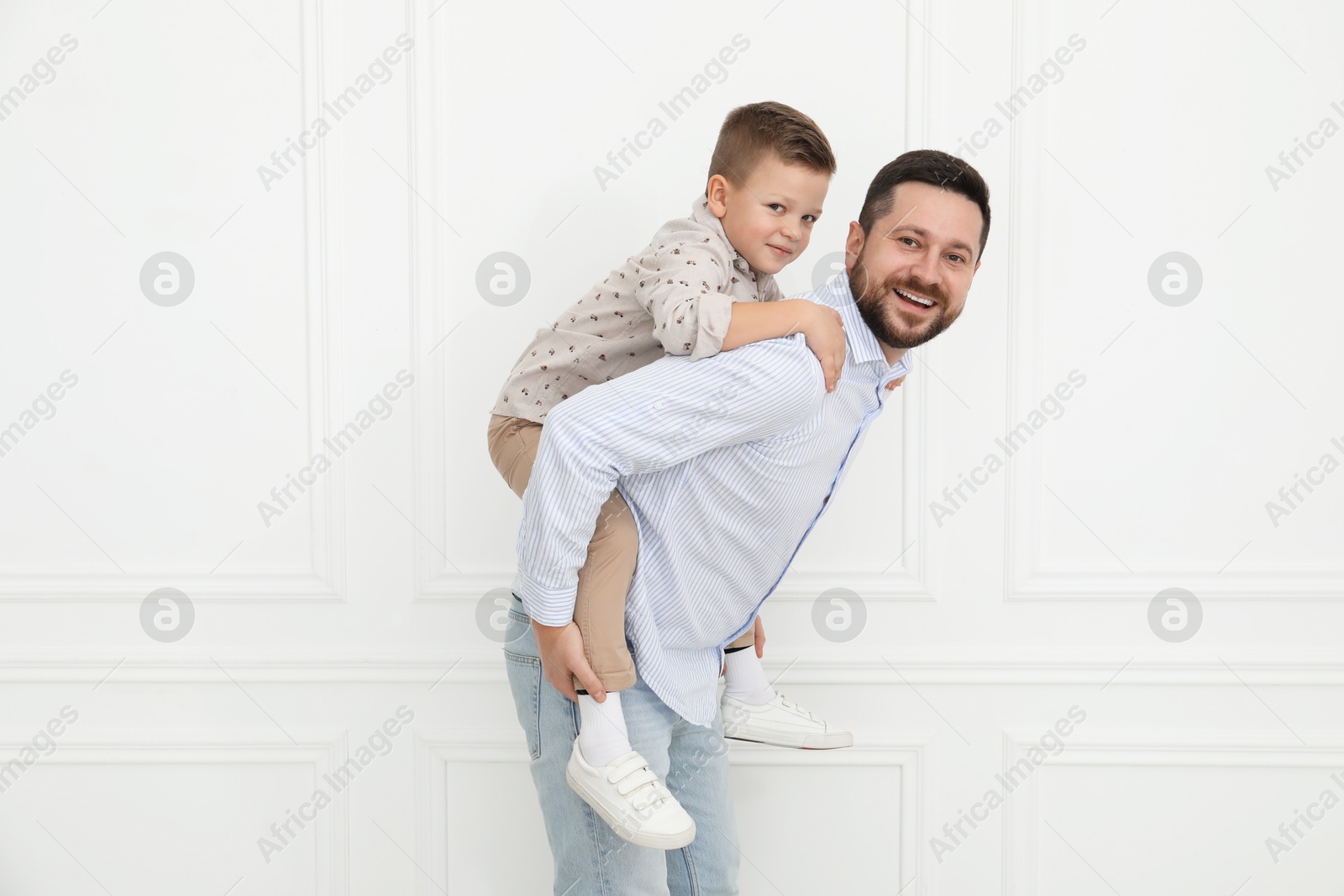 Photo of Happy father and his cute little son near white wall indoors