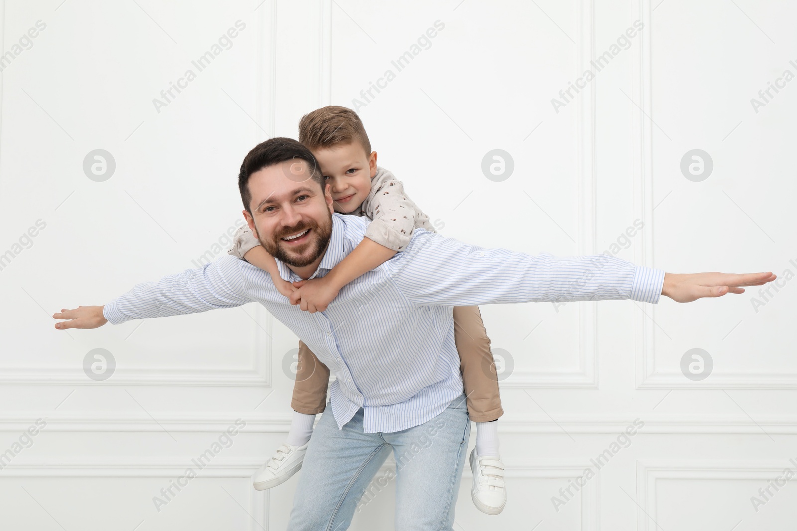 Photo of Happy father and his cute little son near white wall indoors