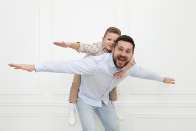 Photo of Happy father and his cute little son near white wall indoors