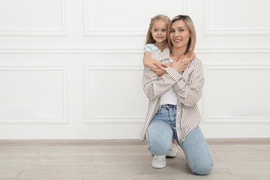 Happy mother and her cute little daughter near white wall indoors