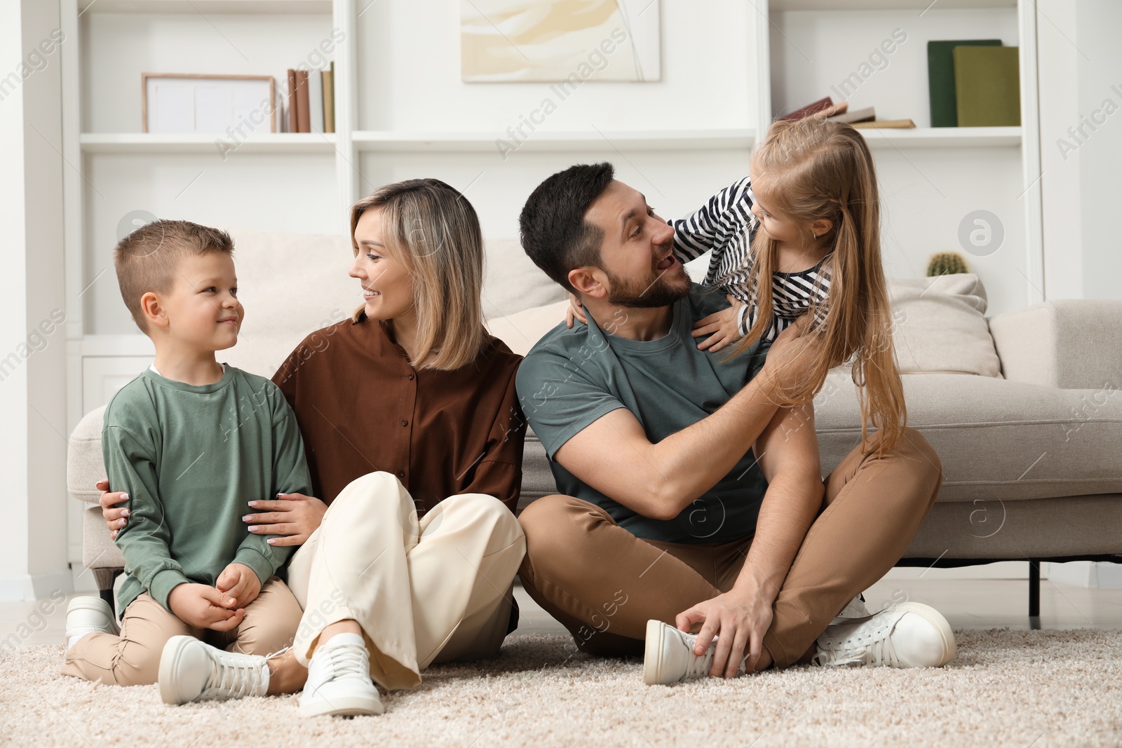 Photo of Happy parents and their children on rug at home