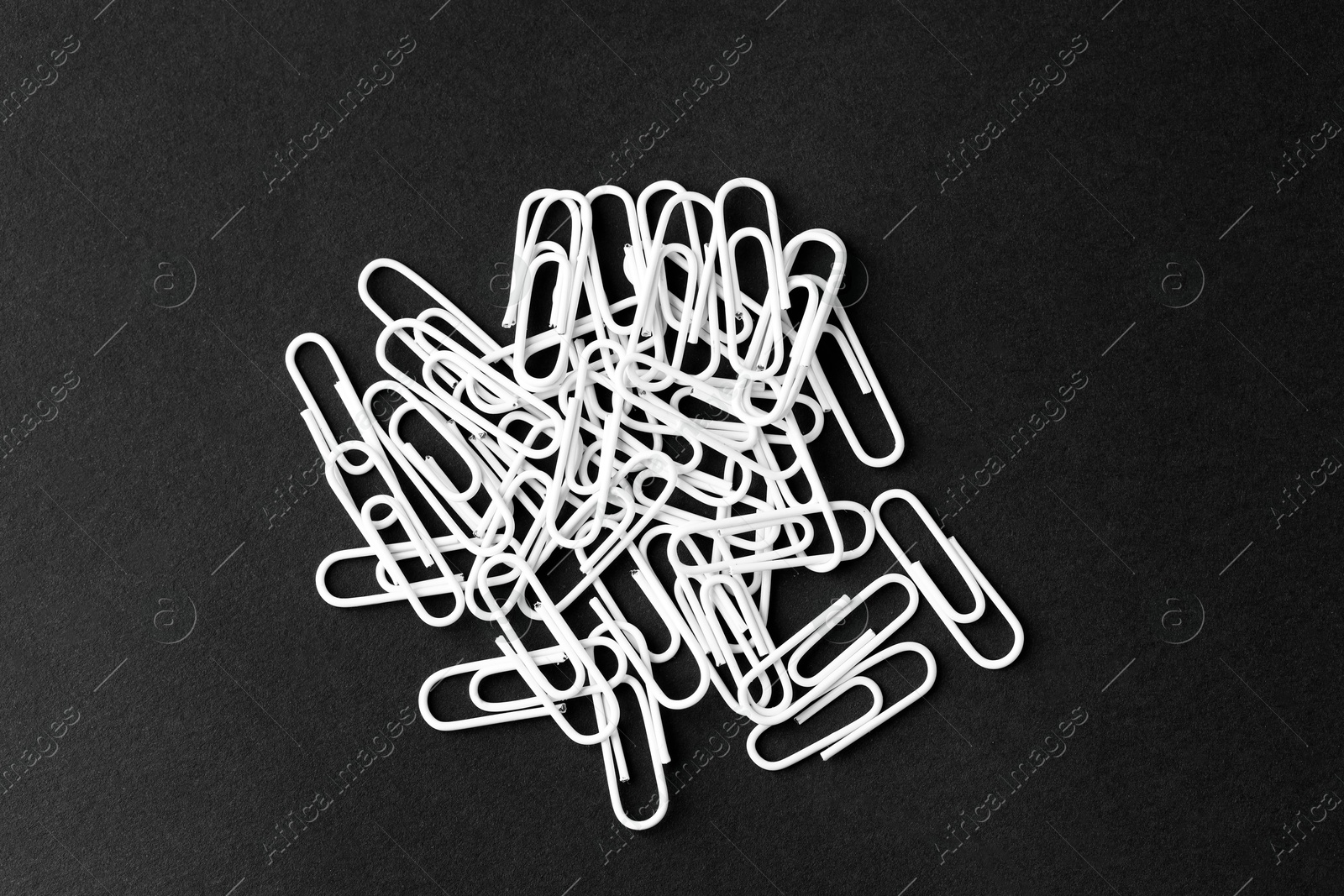 Photo of Many white paper clips on black table, top view