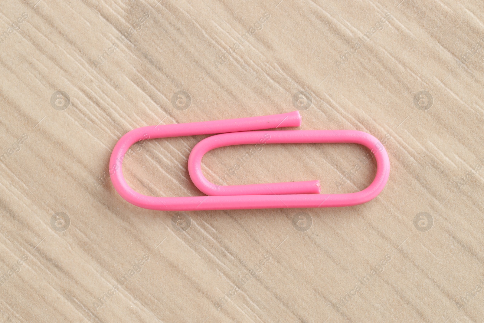 Photo of One pink paper clip on wooden table, top view