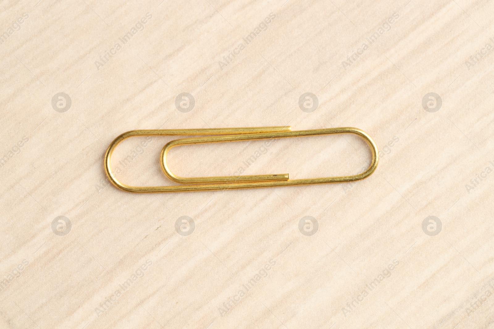 Photo of One golden paper clip on wooden table, top view