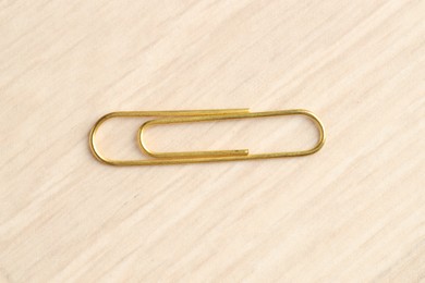 Photo of One golden paper clip on wooden table, top view