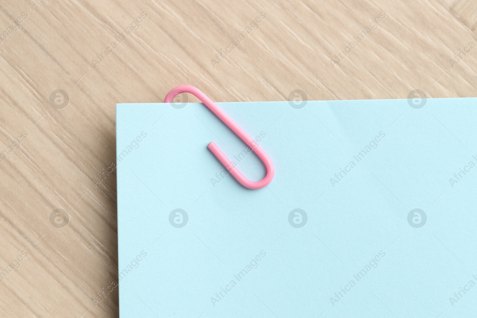 Photo of Paper note with clip on wooden table, top view. Space for text