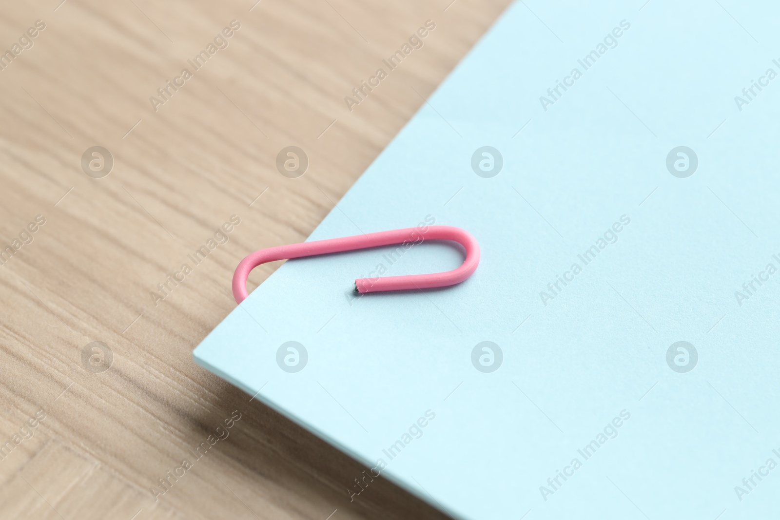 Photo of Paper note with clip on wooden table, closeup. Space for text