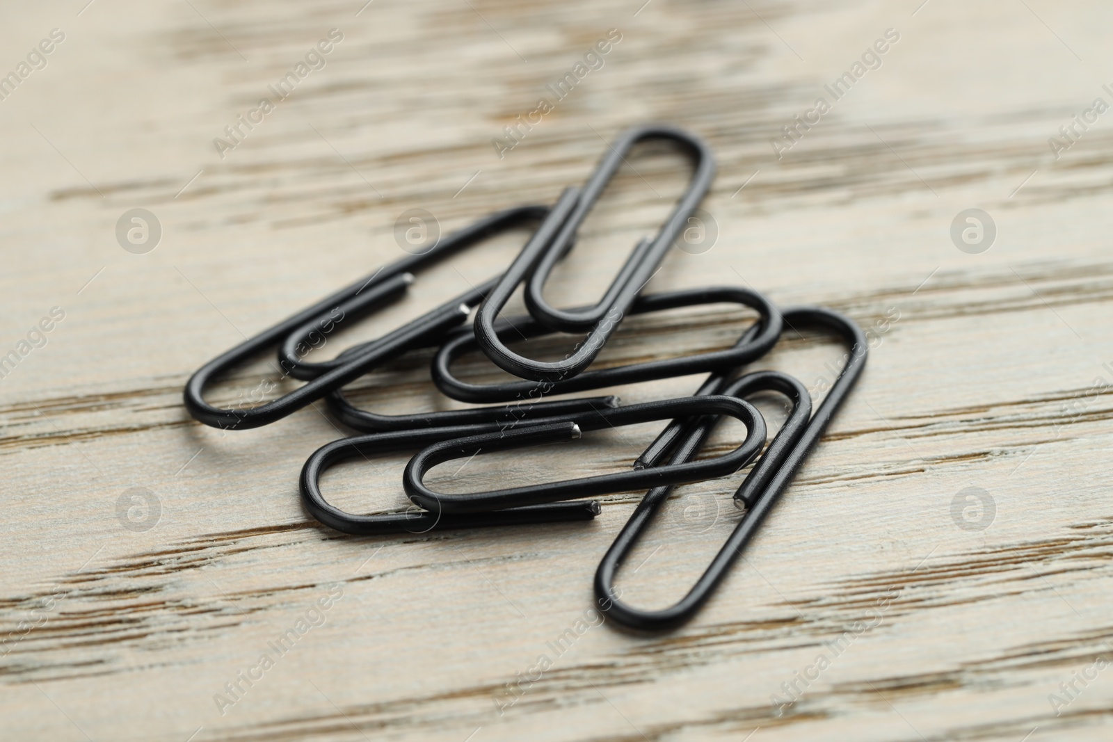 Photo of Many black paper clips on wooden table, closeup