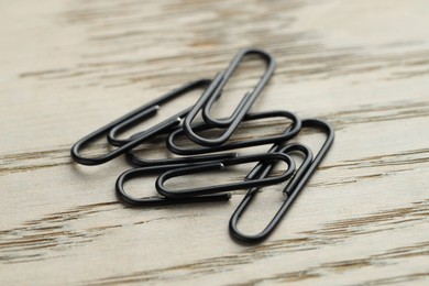 Many black paper clips on wooden table, closeup