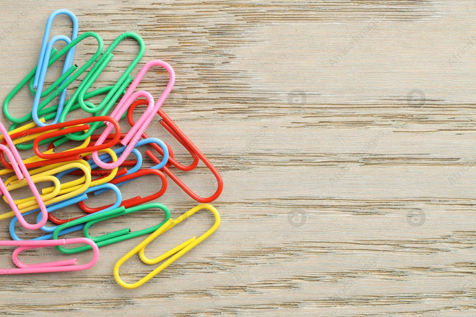 Photo of Many colorful paper clips on wooden table, top view. Space for text