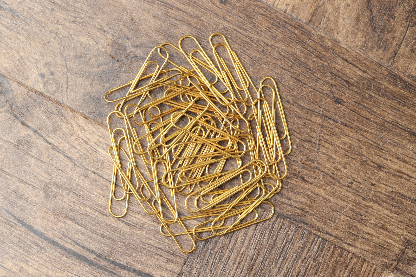 Photo of Many golden paper clips on wooden table, top view