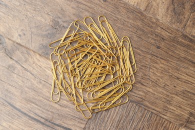 Photo of Many golden paper clips on wooden table, top view