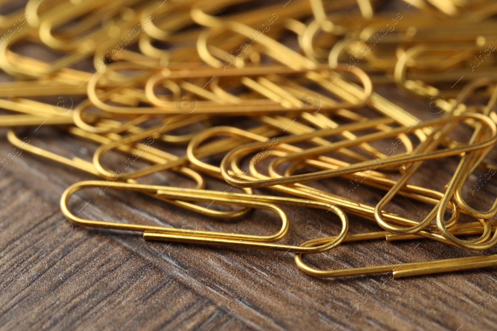 Photo of Many golden paper clips on wooden table, closeup