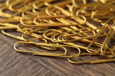 Photo of Many golden paper clips on wooden table, closeup