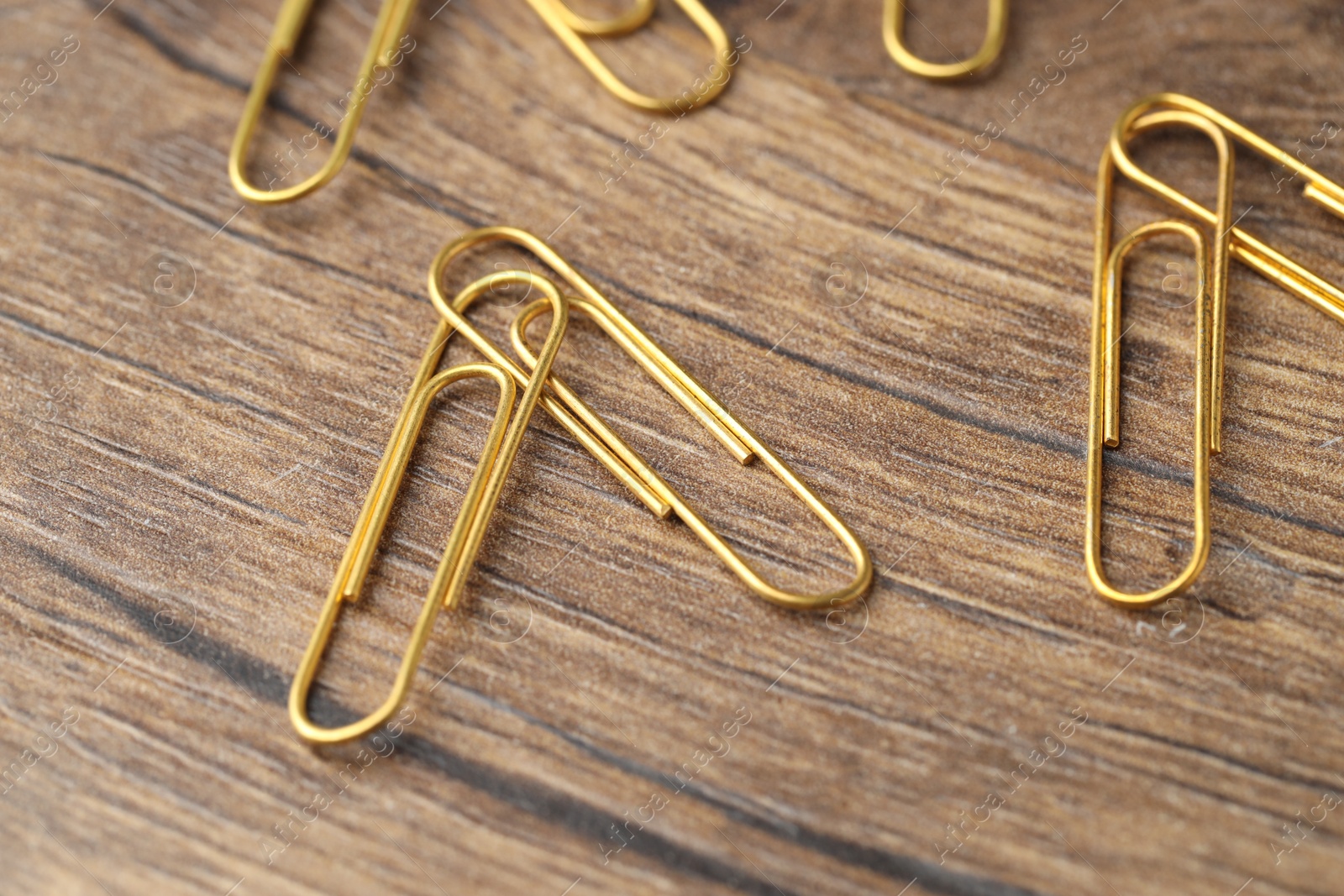 Photo of Many golden paper clips on wooden table, closeup