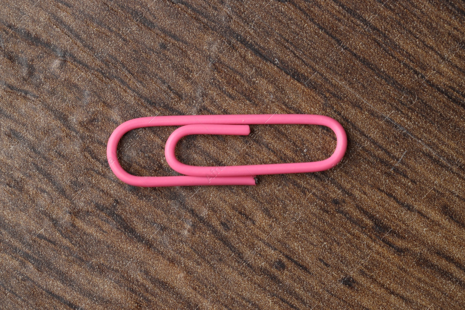 Photo of One pink paper clip on wooden table, top view