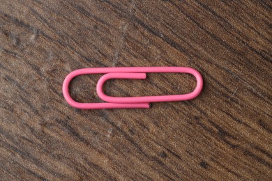 Photo of One pink paper clip on wooden table, top view