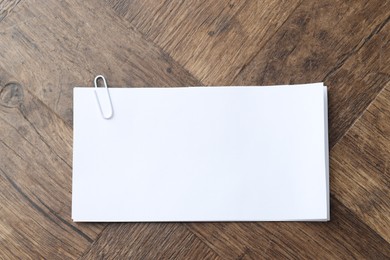 Photo of Paper notes with clip on wooden table, top view. Space for text