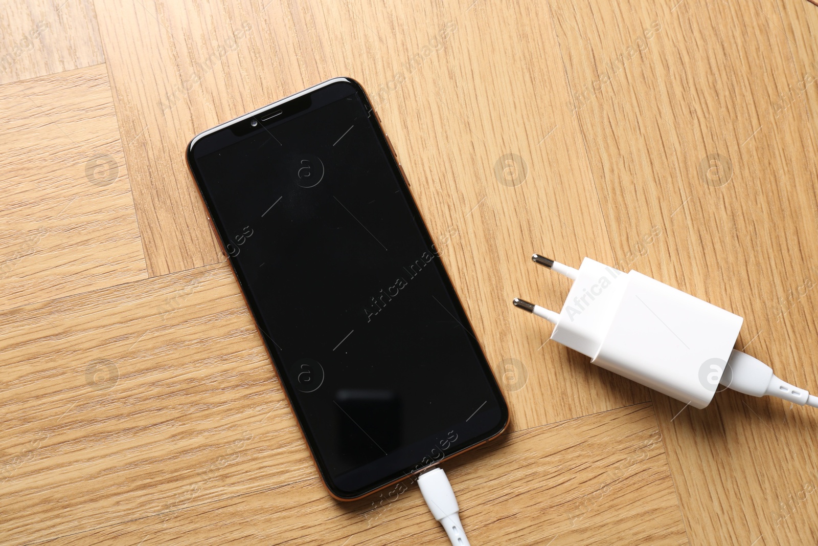 Photo of USB power adapter with charge cable connected to smartphone on wooden table, top view