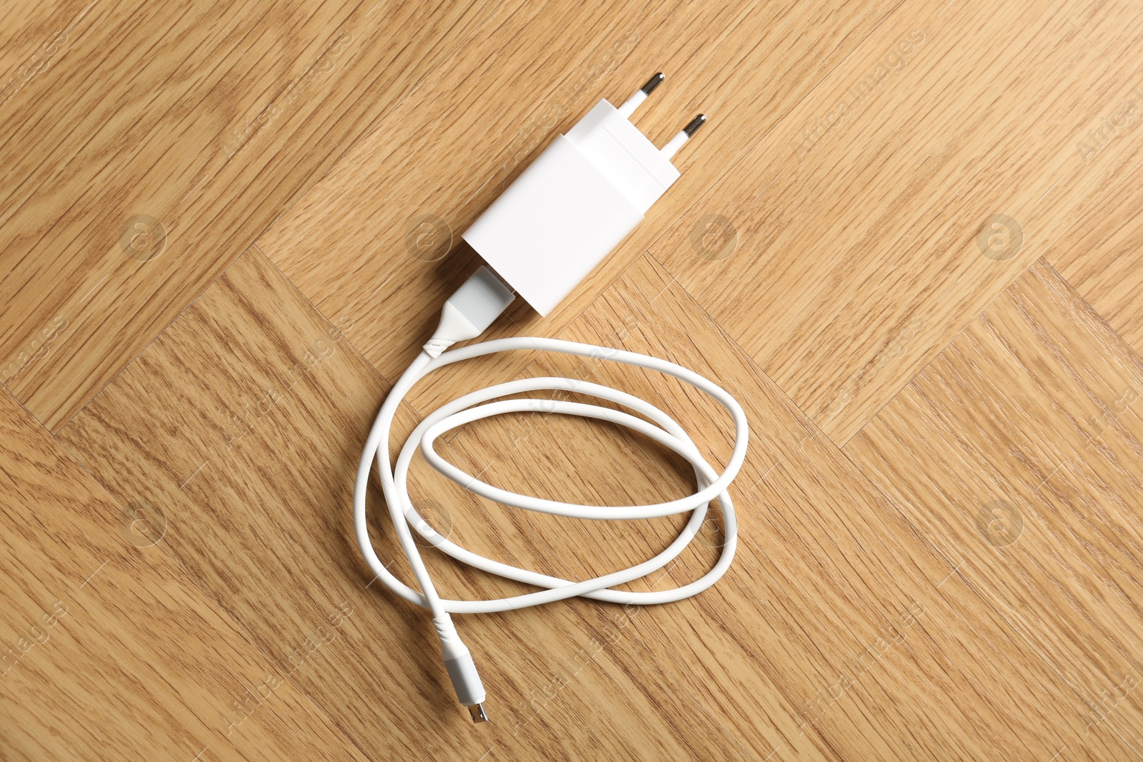 Photo of USB power adapter with charge cable on wooden table, top view