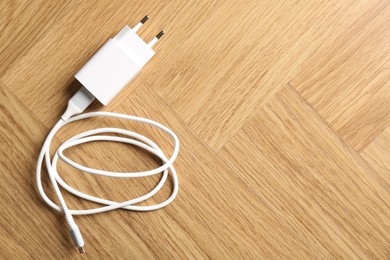 Photo of USB power adapter with charge cable on wooden table, top view. Space for text