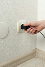 Photo of Woman plugging USB power adapter with charge cable into electrical socket indoors, closeup